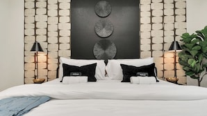 A modern bedroom with a large bed, black and white bedding, a decorative wall panel, and two bedside lamps.