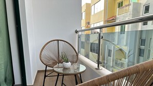 Parvekkeella on rottinkituoleja, lasipöytä ja näkymä keltaiselle rakennukselle.
