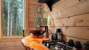 Een keuken met een houten aanrecht, een gasfornuis, een hangende glazen pot en een raam met uitzicht op een bos.