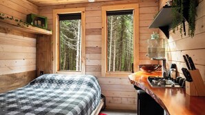 Een gezellig chalet met een bed, een keukenhoek en grote ramen met uitzicht op het bos.