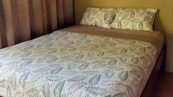 Uma cama com colcha e travesseiro estampados com folhas, e cabeceira de madeira.