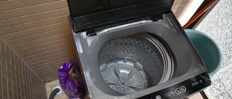 A compact, modern washing machine with a control panel, situated in a small laundry room with tiled walls and a visible water inlet hose.
