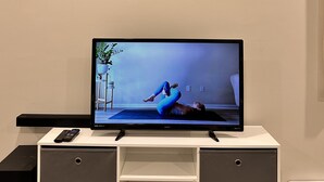 A flat-screen TV on a white entertainment unit with a clock above it. - 1 bedroom in-home mini apartment in Dieppe 5 min drive to the airport WIFI (Dieppe)