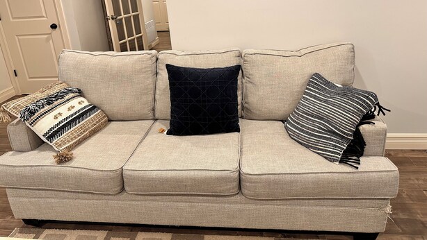 A beige sofa with three cushions, a patterned throw, and a door in the background. - 1 bedroom in-home mini apartment in Dieppe 5 min drive to the airport WIFI (Dieppe)