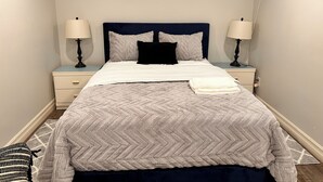 A neatly made bed with a white and blue headboard, two bedside lamps, a folded white towel, and a framed landscape picture on the wall. - 1 bedroom in-home mini apartment in Dieppe 5 min drive to the airport WIFI (Dieppe)