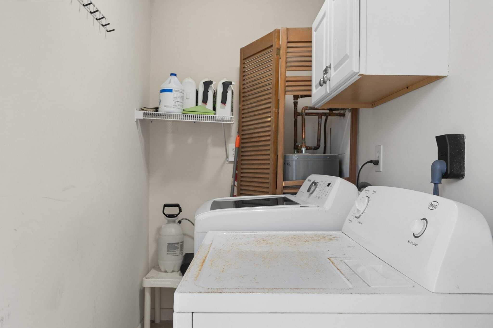 A laundry area with two washing machines, a shelf with cleaning supplies, and a water heater.