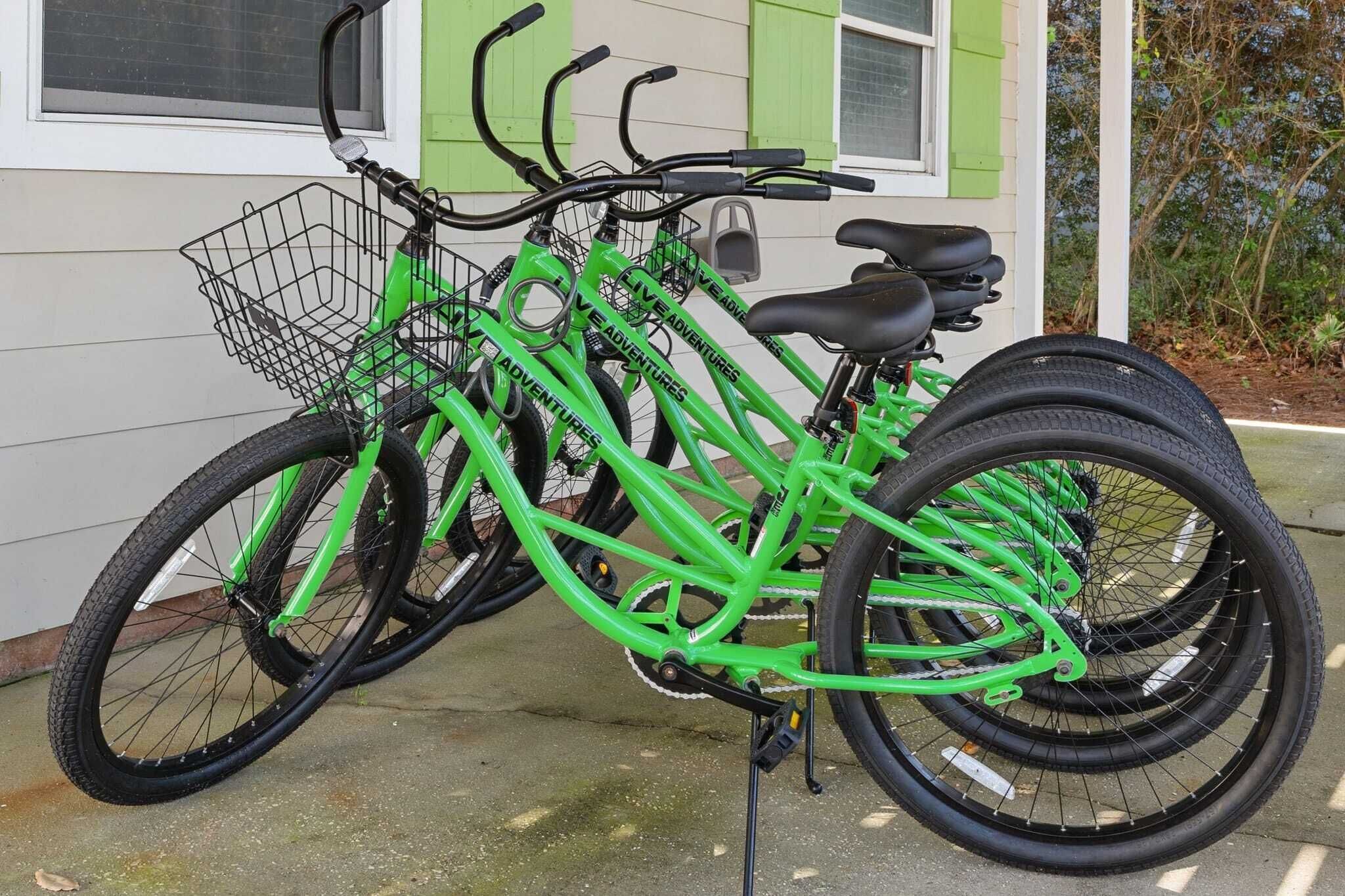 Una bicicleta tándem verde con una cesta, estacionada frente a una casa con puerta y ventanas verdes.