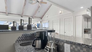 Una cocina con encimeras de granito, cafetera, licuadora y ventilador de techo.