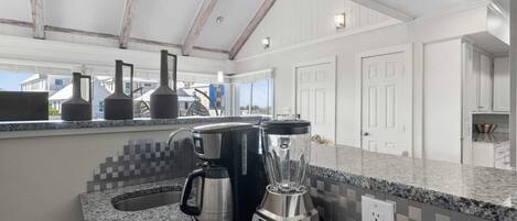 A kitchen with granite countertops, a coffee maker, a blender, and a ceiling fan.
