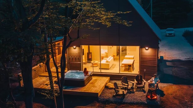 Uma cabana moderna com hidromassagem, área de estar externa e uma grande porta de vidro que dá para o interior.