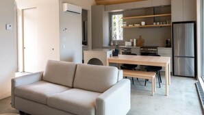 Um espaço de estar moderno com teto de madeira, sofá, mesa de jantar e área de cozinha com frigorífico e armários.