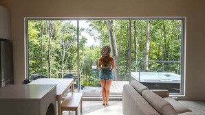 Interior moderno com uma grande porta de vidro deslizante que dá para uma vista da floresta, um sofá, uma mesa de jantar e uma cozinha.