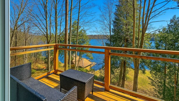 A wooden deck with wicker furniture overlooking a lake surrounded by trees.