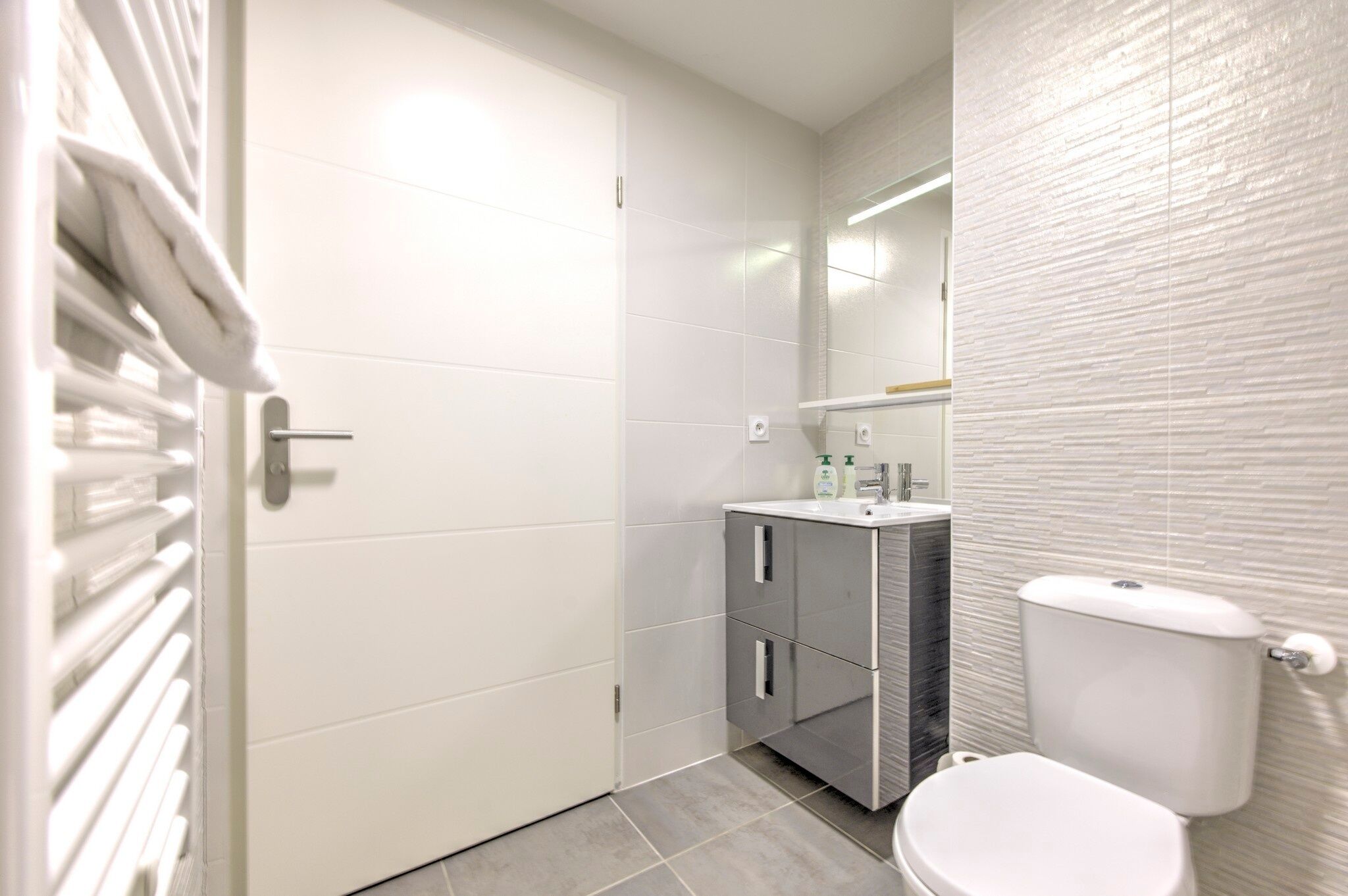 Une petite salle de bain moderne avec des toilettes blanches, un meuble-lavabo avec un miroir et un porte-serviettes.