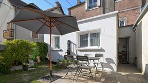 Une terrasse avec une table et des chaises, un grand parasol et des plantes en pot.