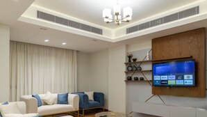 Una sala de estar moderna con un televisor de pantalla plana montado en la pared, un juego de sofá, una mesa de centro y un estante decorativo con objetos.