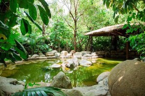 Ein friedlicher Garten mit Teich, Steinen und einem strohgedeckten Gebäude.