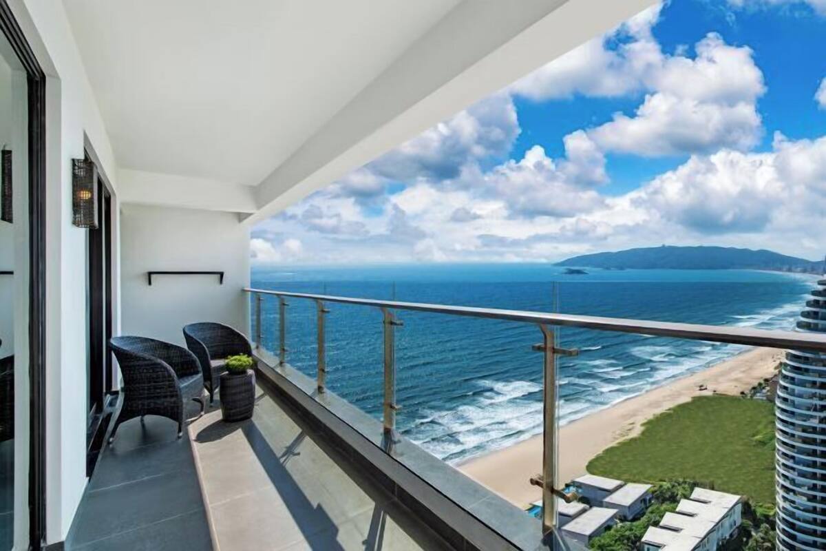 A balcony with a view of the ocean, a beach, and distant mountains.