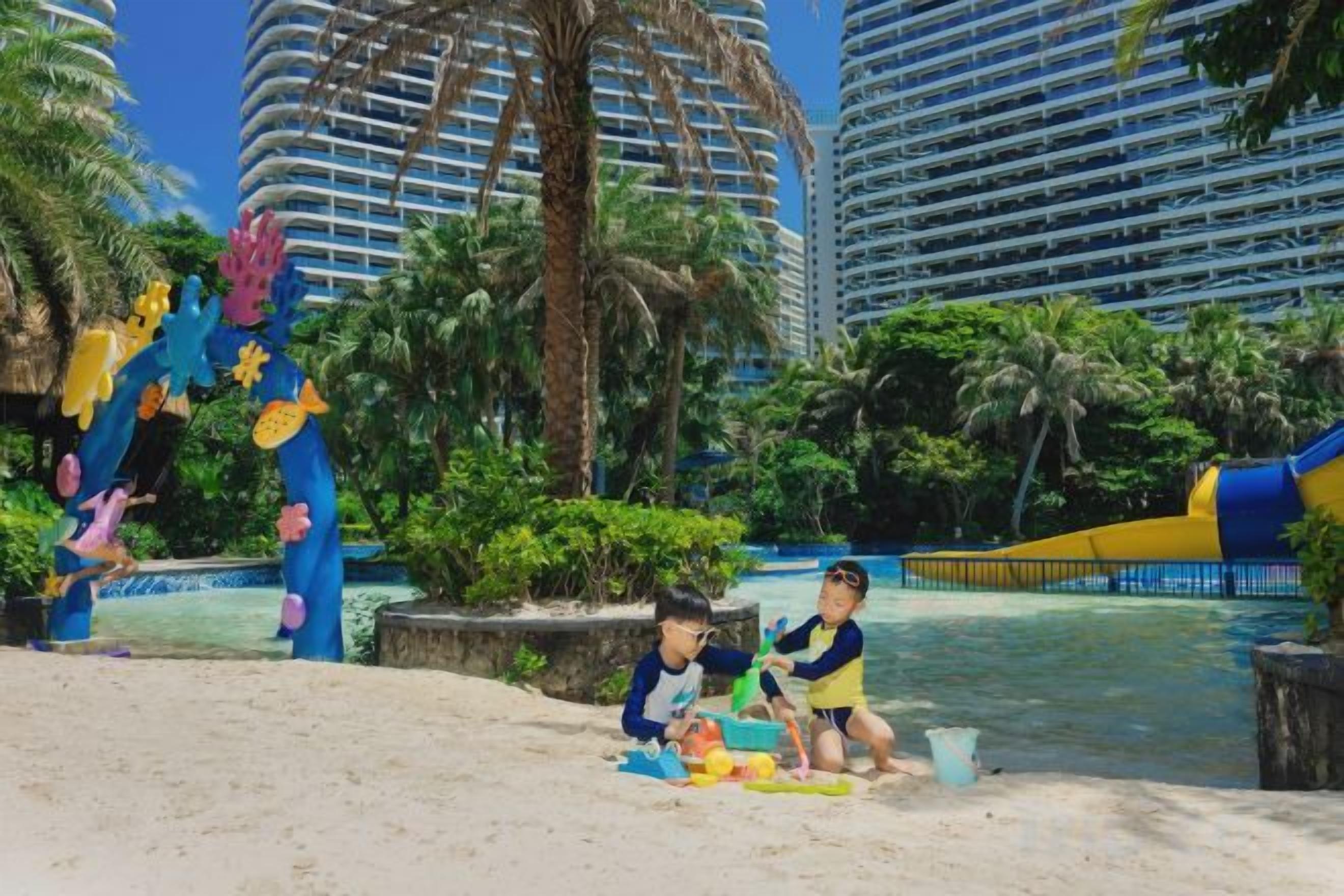 A beach area with palm trees, a water slide, and a pool.