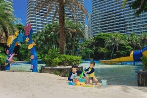 Ein Strandbereich mit Palmen, einer Wasserrutsche und einem Pool.