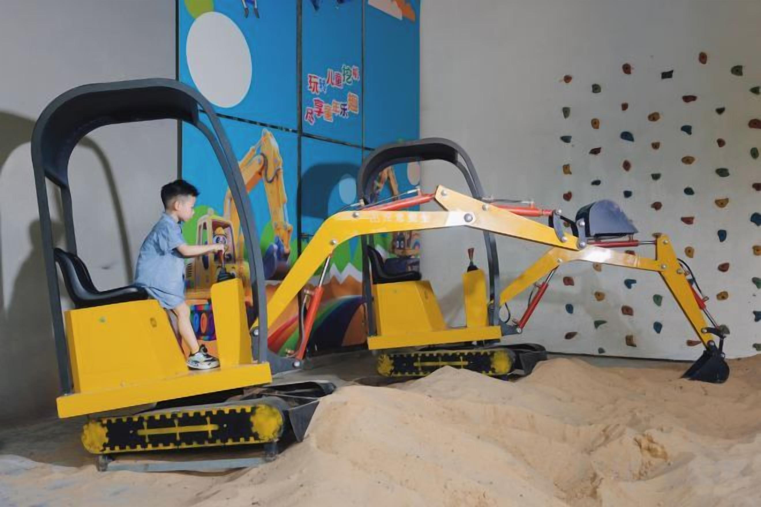 Un niño manejando una excavadora amarilla de juguete en un área de juegos con arena.