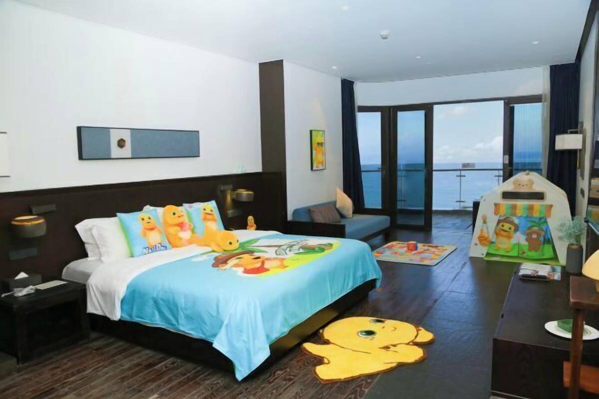 A modern hotel room with a large bed, a balcony with a view, and a children's play area.