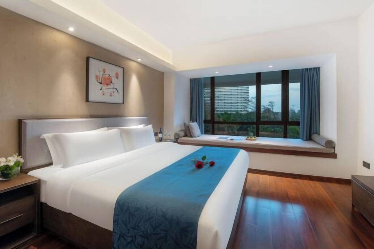 A modern hotel room with a large bed, a window seat, and a view of the city.