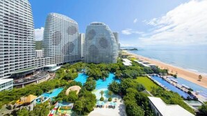A resort with multiple high-rise buildings, a central pool surrounded by lush greenery, and a beach area.