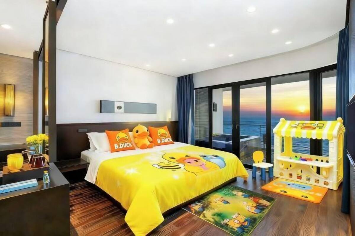 A hotel room with a bed, a toy arcade, a view of the sunset, and a window.