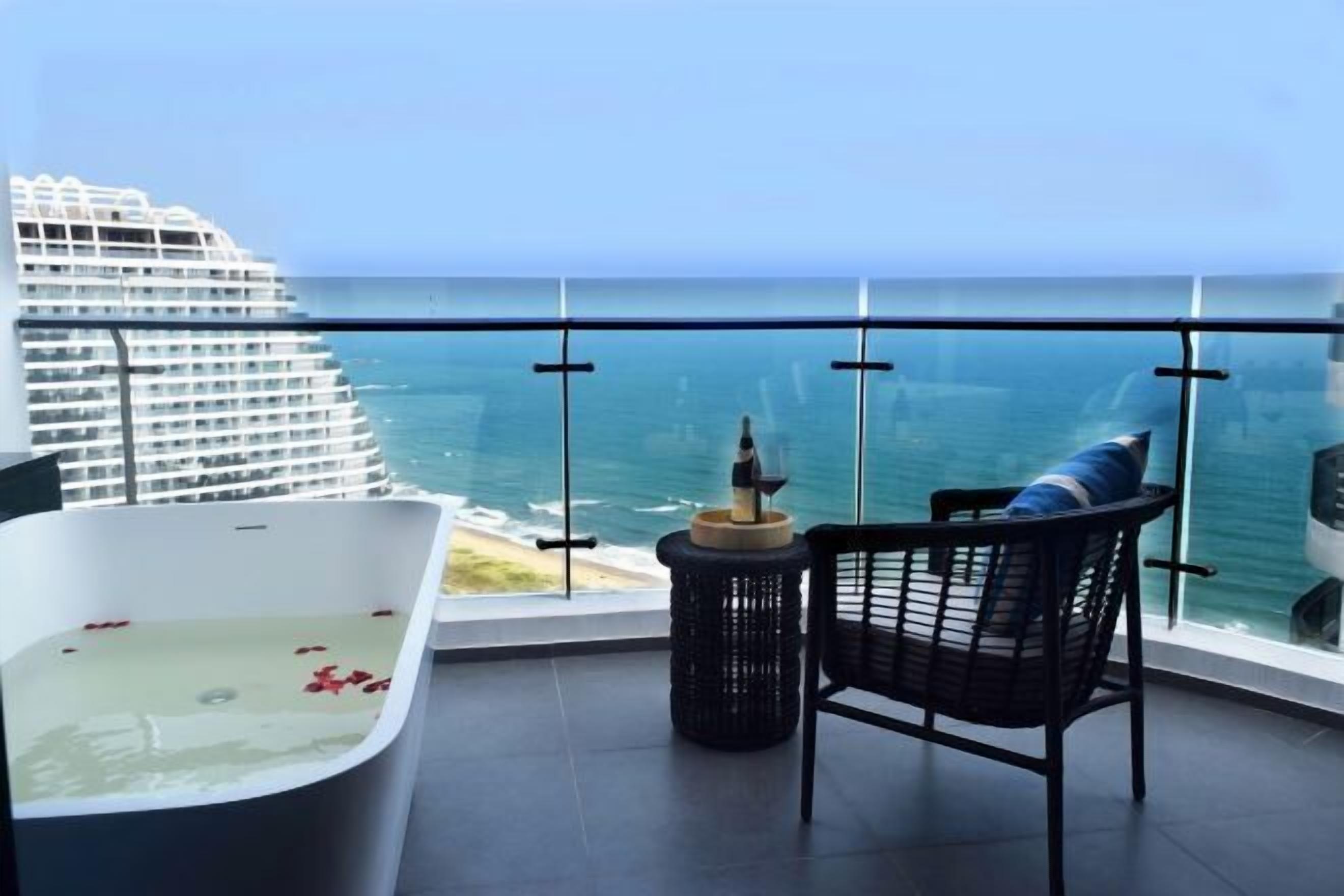 A balcony with a view of the ocean, a bathtub, and a chair.
