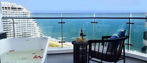 A balcony with a view of the ocean, a bathtub, and a chair.