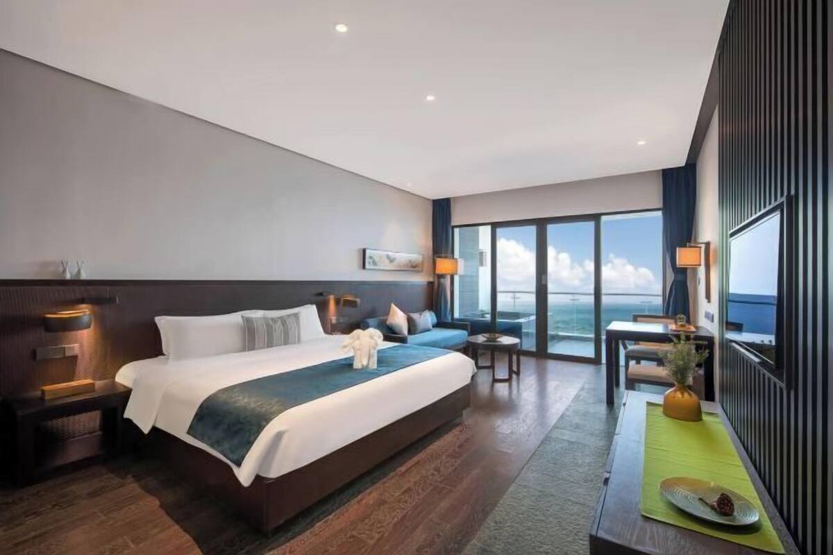 A modern hotel room with a large bed, a dining area, and a view of the sky.