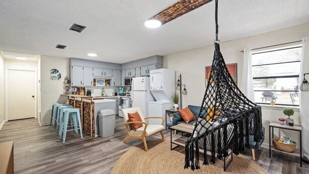 A compact living space with a kitchenette, a hanging macrame chair, and a round woven rug. - Cozy duplex w/fire pit & BBQ (Pensacola)