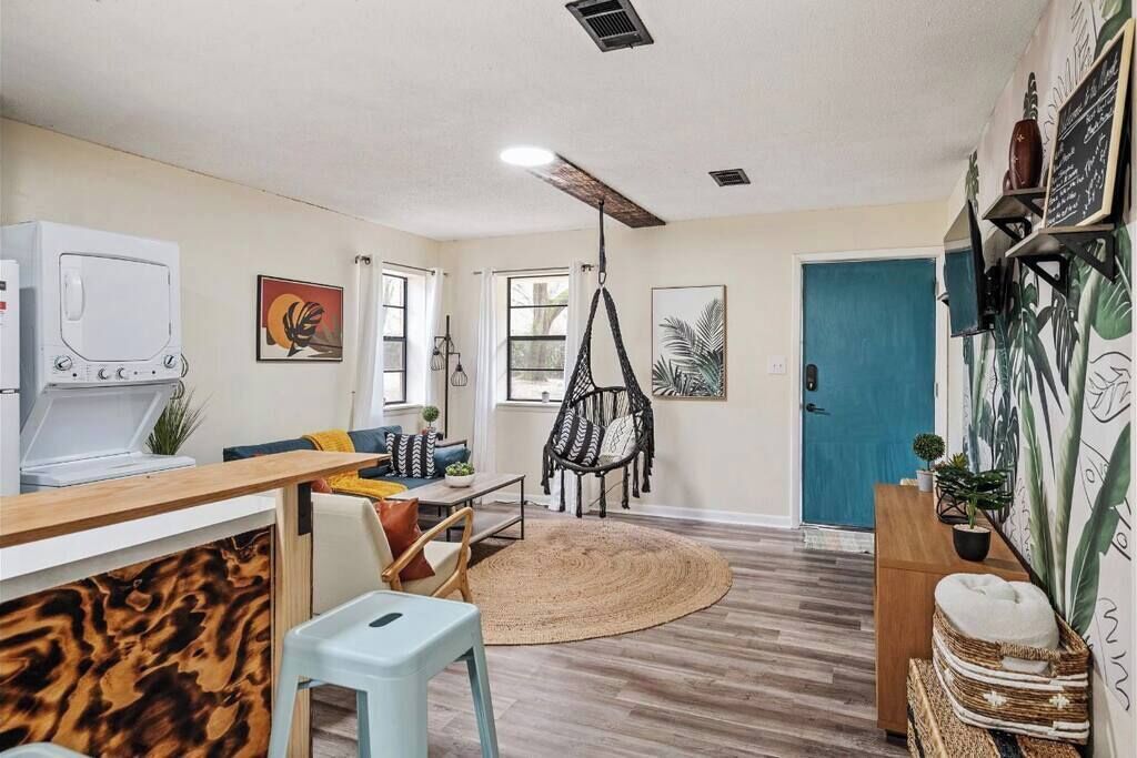 A modern living room with a wooden floor, a sofa, a hanging chair, a dining table, and a television.