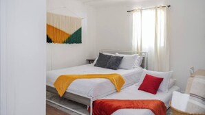 Uma cama de solteiro com cabeceira branca, manta amarela, travesseiro vermelho e travesseiro cinza.