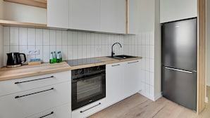 A modern kitchen with white cabinets, a stainless steel refrigerator, a built-in oven, and a wooden countertop. - Horizon 122 -SeaView by GrandApartments  (Gdansk)