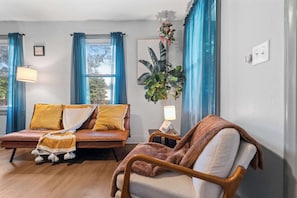 Un salón con un sofá de cuero marrón, una silla de madera, una planta en maceta y un cuadro en la pared.