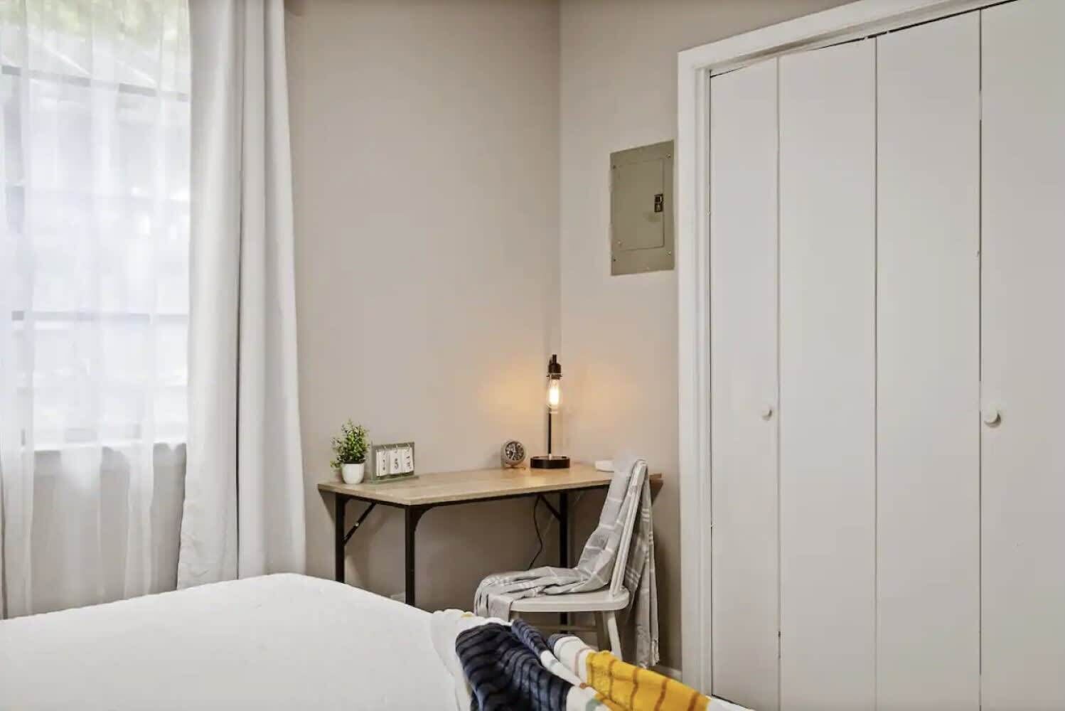 Un dormitorio con cama, escritorio con lámpara, silla y armario.