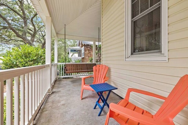 A covered porch with a bench, two chairs, and a table.