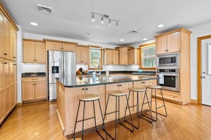 Una cocina moderna con armarios de madera, electrodomésticos de acero inoxidable y una isla central con taburetes de bar.