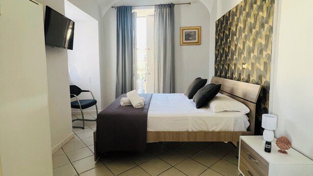 A hotel room with a bed, bedside table, TV, and a view of the outdoors. - Rooms for Vacation and Relaxation. City Center SORRENTO Coast (Vico Equense)