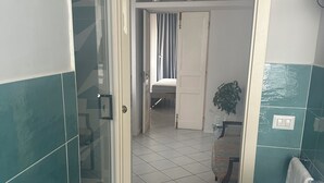A bathroom with a bathtub, a shower, and a sink. There is a door leading to a bedroom with a bed and a curtain. - Rooms for Vacation and Relaxation. City Center SORRENTO Coast (Vico Equense)