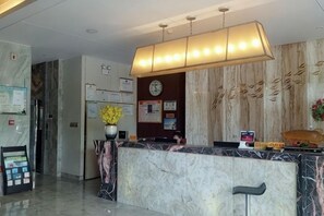 A hotel reception area with a marble counter, a clock, and framed notices on the wall. - Kaiwei Hotel (Wanning High-speed Railway Station Branch) (Wanning)