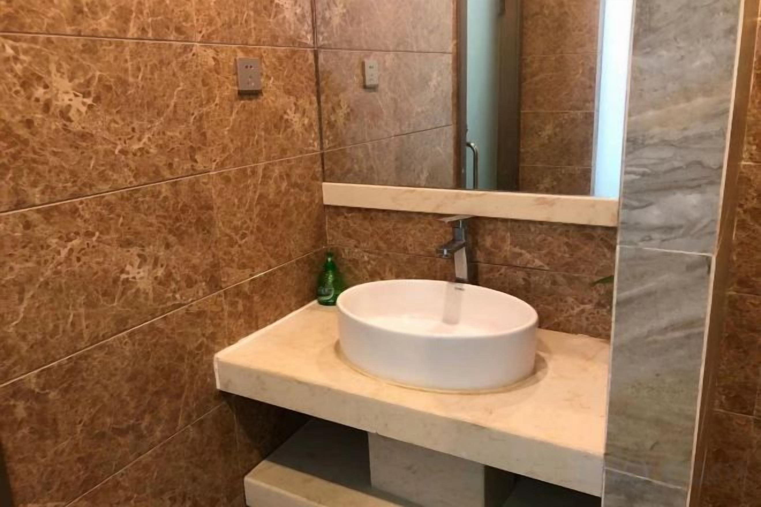 A bathroom with a marble wall, a white sink, and a mirror above it.