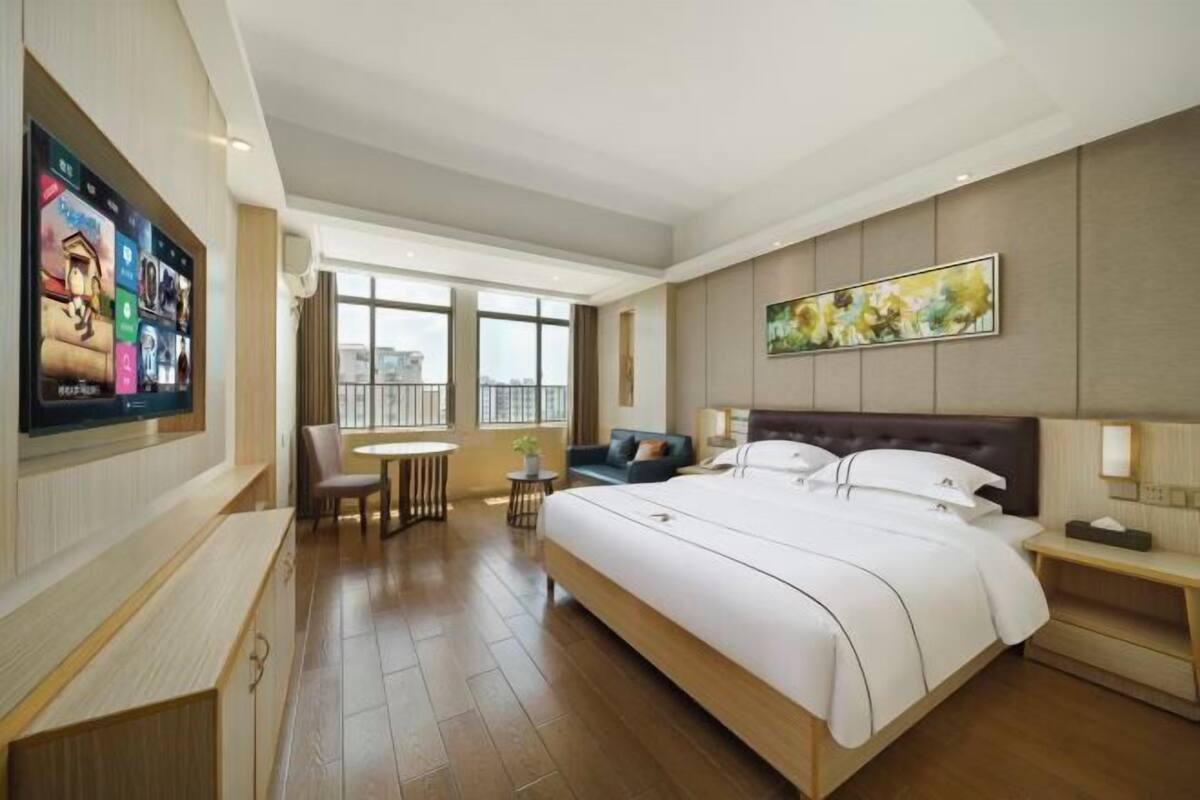 A hotel room with a large bed, a TV mounted on the wall, a dining table, and a sofa.