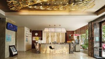 A hotel lobby with a reception desk, a clock, and a television screen.
