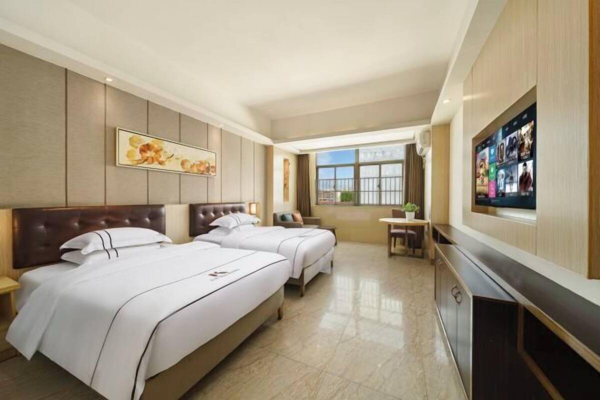 A hotel room with two beds, a TV, a desk, and a window with a view.