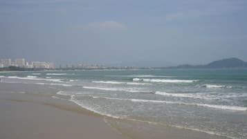 Praia com ondas, paisagem urbana ao longe e uma montanha.