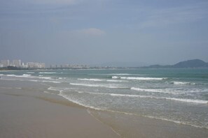 A beach with waves, a distant cityscape, and a mountain. - Kaiwei Hotel (Wanning High-speed Railway Station Branch) (Wanning)