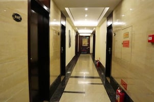 Un pasillo de hotel con puertas, un extintor y señales de salida de emergencia.